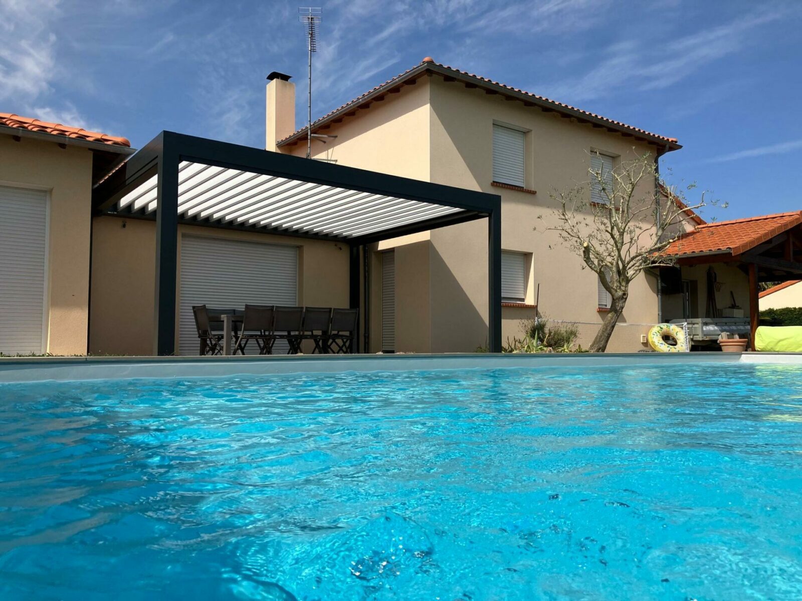 pergola bioclimatique ouverte le long d'une maison moderne avec vue sur l'eau turquoise de la piscine à cholet