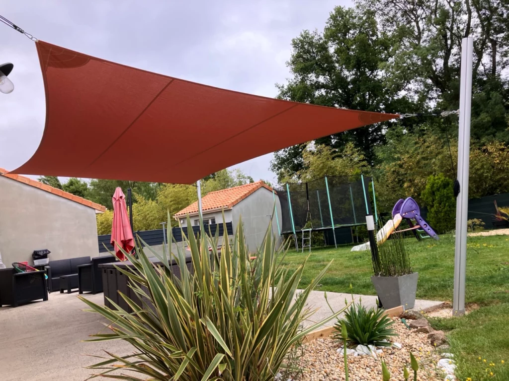 voile d'ombrage rouge donnant sur un extérieur de maison avec massif et plantes, gazon