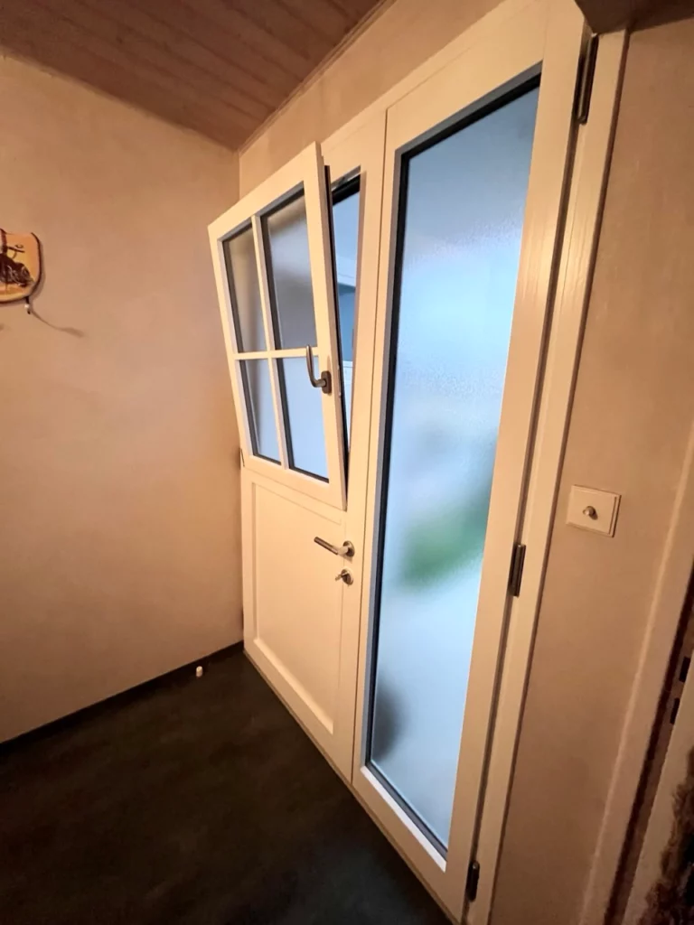 vue d'une porte d'entrée mixte bois alu du côté d'une entrée de maison a cholet. C'est une porte blanche intérieur avec un ouvrant dans l'ouvrant , la partie supérieur de la porte est ouverte en oscillo battant
