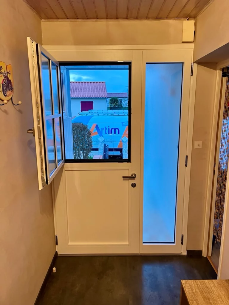 vue d'une porte d'entrée mixte bois alu d'une entrée de maison a cholet. C'est une porte blanche intérieur avec un ouvrant dans l'ouvrant , la partie supérieur de la porte est ouverte et on voit à travers l'ouvrant ouvert un camion artim dans la rue