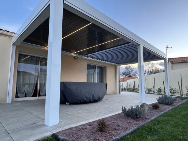 pergola bioclimatique blanche sur une terrasse avec table, pouzzolane lames fermées laissant voire les led à cholet