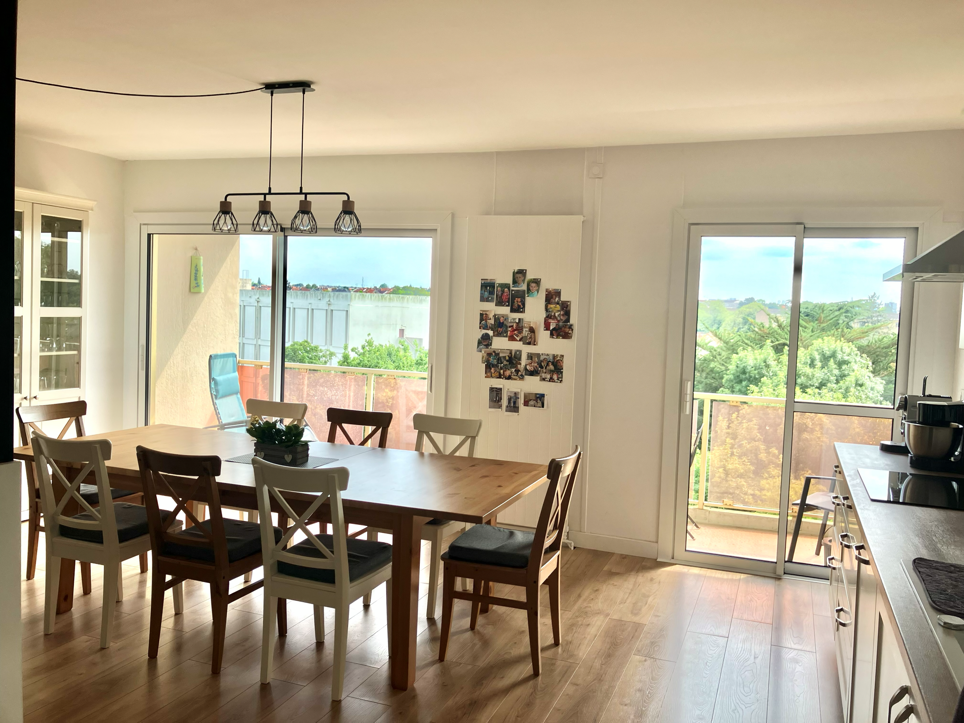 Salle à manger lumineuse avec deux grandes baies vitrées coulissantes blanches donnant sur balcons et extérieur à Cholet.