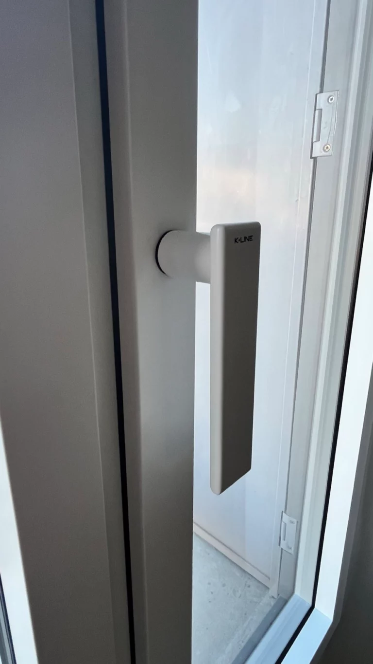 Gros plan sur une poignée de fenêtre blanche K-LINE vue de l’intérieur, dans une habitation à Cholet.