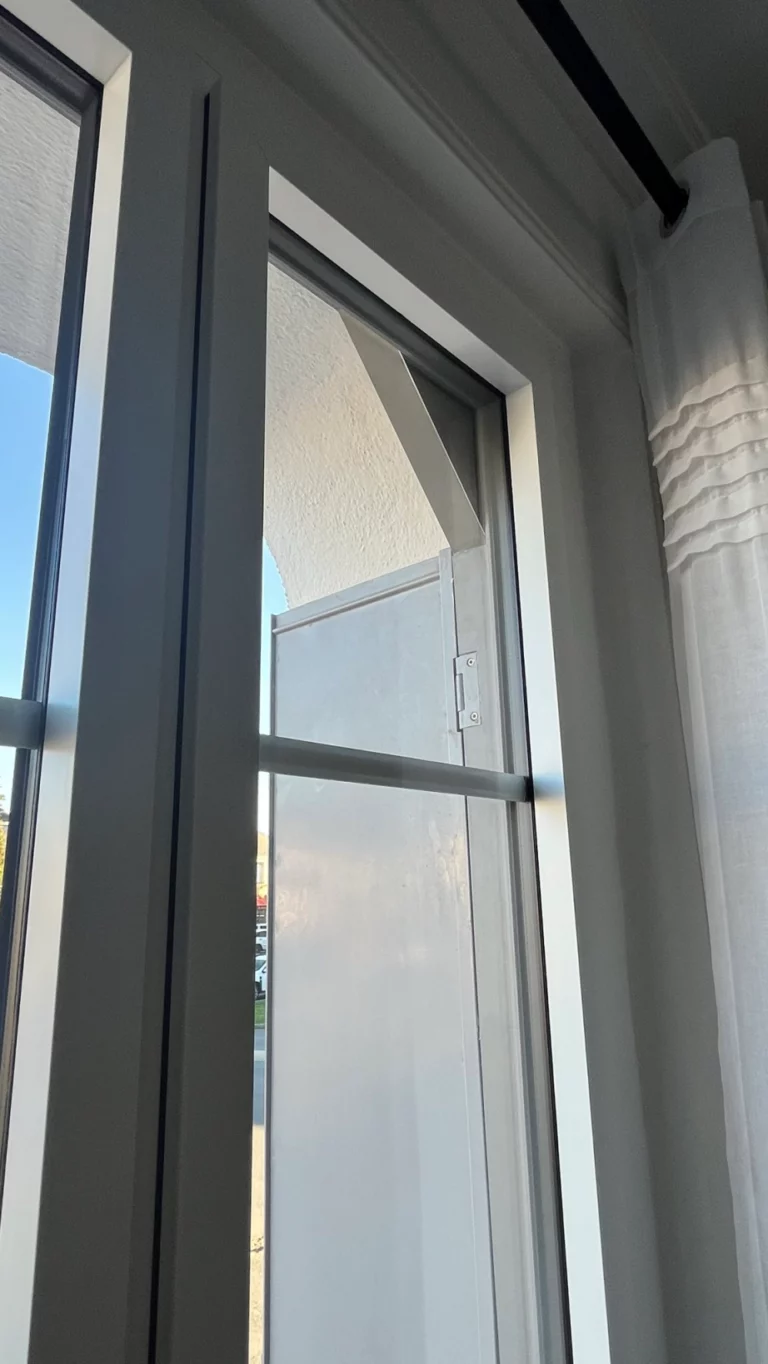 Détail d’une fenêtre blanche avec petit ouvrant et volet extérieur, vu depuis l’intérieur d’une pièce à Cholet.