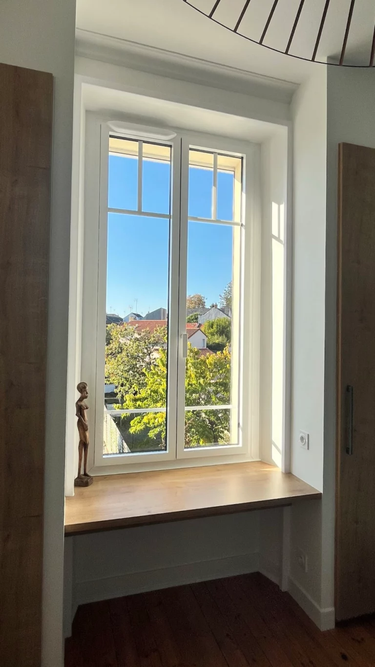 Fenêtre blanche à deux vantaux dans une niche intérieure avec tablette bois et vue sur les toits à Cholet.