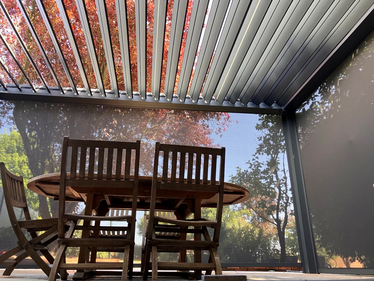 Terrasse couverte par pergola bioclimatique, vue sur jardin et lames réglables