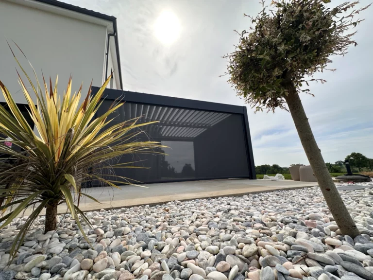 Pergola bioclimatique avec lames orientables ouvertes sur une terrasse avec vue jardin