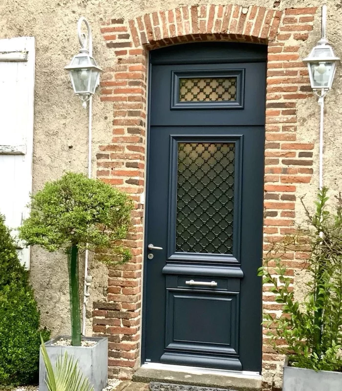 porte d'entrée en alu bleu foncé avec grille dans le vitrage pour une maison de caractère avec briques